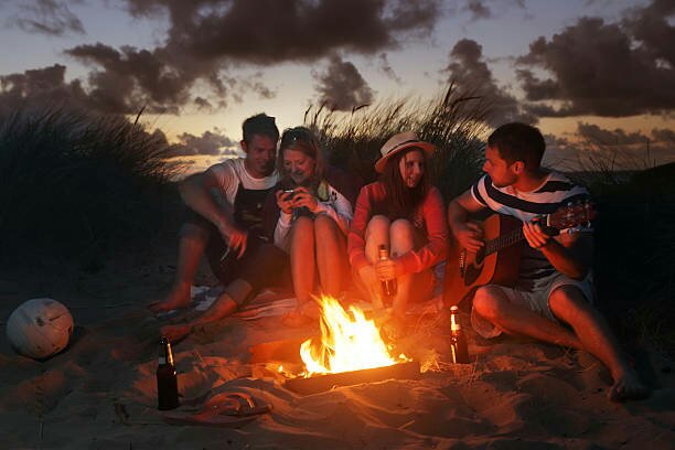 Young adults sitting around camp fire on sand dunes